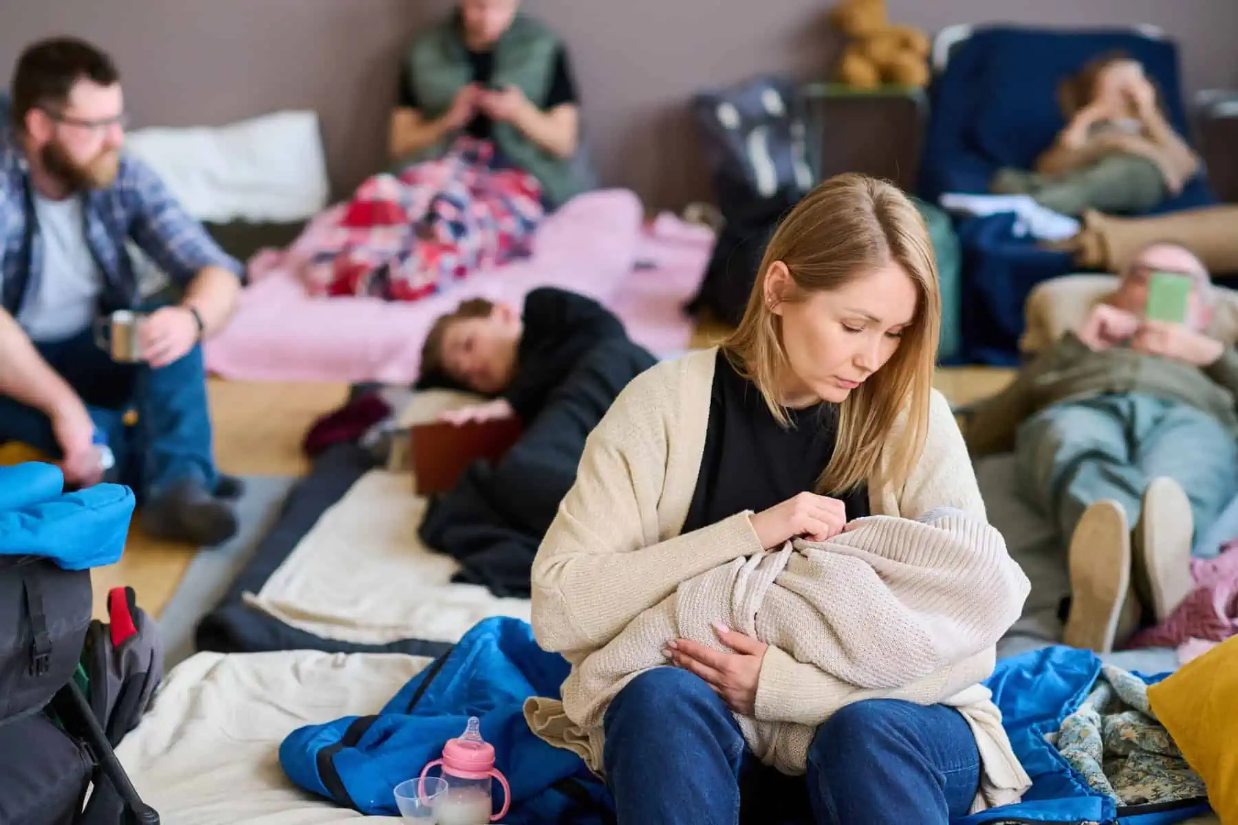 young-blond-female-refugee-lulling-baby-wrapped-into-warm-plaid-on-bed